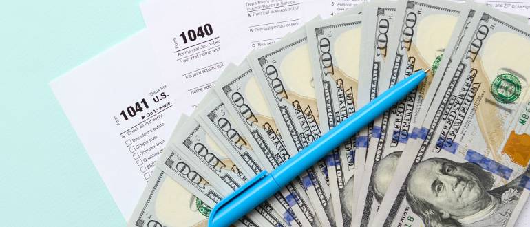Tax forms lies near hundred dollar bills and blue pen
