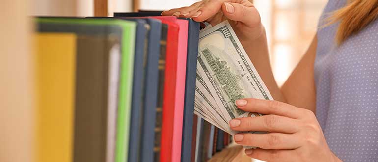 Woman hiding money between books on shelf indoors